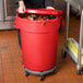 A woman holding a red 32 gallon mobile ingredient storage container full of food.