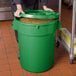 A woman holding a green 32 gallon ingredient storage bin with a lid full of corn.