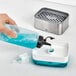 A hand pouring blue liquid into a white OXO sponge holder.