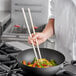 A chef cooking vegetables in a pan with Emperor's Select bamboo chopsticks.