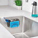 An OXO Good Grips stainless steel sink caddy holding a blue sponge and white brush.