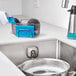 An OXO stainless steel sink caddy holding a blue sponge and brush over a kitchen sink.