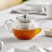A clear glass Acopa Lotus teapot filled with clear liquid on a table.