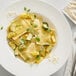 A plate of ravioli pasta served with sliced zucchini, yellow squash, fresh herbs, and a sprinkle of cheese seasoning.