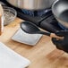 A person in black gloves using a black Tablecraft Sierra square spoon rest to place a spoon on a counter.