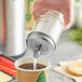 A hand pouring sugar from a Tablecraft beehive sugar pourer into a cup of coffee.