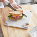 A person cutting a sandwich on a San Jamar white cutting board.
