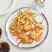 A Choice aluminum pizza pan with fried shrimp and fries on it on a table in a seafood restaurant.