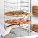 A person holding a pizza on a Choice aluminum pizza pan rack.