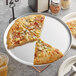 A pizza on a Choice aluminum coupe pizza pan with a slice missing.