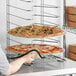 A person putting a Choice pizza on a metal rack.