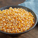 A bowl of Pop Weaver Gold Butterfly popcorn kernels on a blue cloth.