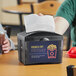 A person using a black OneUp napkin dispenser on a table.