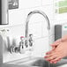 A person washing their hands under a Waterloo wall mount faucet with a gooseneck spout.