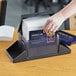 A hand putting a stack of paper napkins into a black plastic dispenser with a condiment caddy.