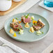 An Acopa Pangea Harbor Blue matte porcelain plate with tuna, cucumber, and a lemon slice on it.