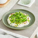 An Acopa Pangea sage matte porcelain plate with green beans and cream cheese on it.