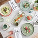 Acopa Pangea sage matte porcelain plates on a table with plates of food and utensils.