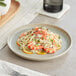 A white Acopa Pangea porcelain plate with pasta, shrimp, and lemon slices on it.