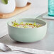 A bowl of soup on a white table with a blue bowl and a spoon.