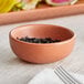 An Acopa Terra Cotta ramekin filled with black salt on a table in a farm-to-table restaurant.