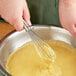 A person using an OXO SteeL narrow piano whisk to mix yellow batter in a bowl.