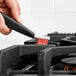 A person using an OXO Good Grips red brush to clean a gas stove.