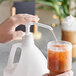 A hand pressing a white Choice liquid pump to pour liquid into a glass.