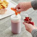 A person using a Choice condiment pump to pour red sauce into a plastic container with a white lid.