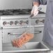 A person in a chef's uniform holding a Main Street Equipment fryer basket with food in it.