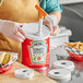 A hand using a Choice condiment pump to dispense ketchup onto a hot dog.