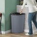 A person in a white shirt and jeans putting a bag in a grey Lavex corner round trash can.