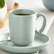 An Acopa Harbor Blue porcelain cup on a saucer with a spoon.