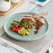 An Acopa Pangea Harbor Blue Matte Porcelain Plate with meat and vegetables on it on a table.