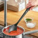 A person using an OXO Good Grips high heat nylon solid spoon to stir red sauce in a pot.