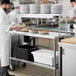 A man in a chef's uniform using a Regency expeditor table to hold plates.