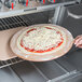 A person using an American Metalcraft round pizza peel to cook a pizza in an oven.