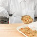 A person in white gloves using a Vollrath black perforated oval Spoodle to serve rice with meat and vegetables from a white container.