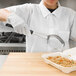 A woman using a Vollrath black metal perforated oval Spoodle to serve food.