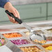 A hand holding a black Vollrath Spoodle over a tray of food.