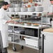 A chef in a white uniform preparing food on a Regency expeditor table with undershelves.