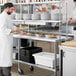 A man in a white coat standing at a stainless steel Regency work table holding a plate of food.
