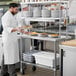 A chef in a kitchen using a Regency stainless steel expeditor table.