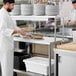A chef in a white coat standing at a Regency work table holding plates of food.