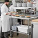 A chef in a white coat and gloves using a Regency expeditor table to plate food.