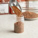 A metal scoop pouring brown seasoning into a clear plastic jar.