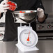 A person weighing tomatoes in a bowl on a Cardinal Detecto mechanical scale.