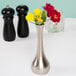 A Tablecraft metal tear drop bud vase with red flowers on a table.