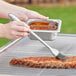 A person using a Backyard Pro silicone basting brush to baste ribs on a barbecue grill.