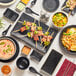 A table with Acopa Izumi black and white melamine bowls filled with rice and vegetables, with a black spoon next to them.